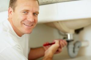 a San Mateo CA plumbing contractor tightens a bathroom sink drain line with a crescent wrench