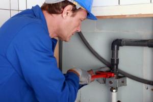 a certified plumber in San Mateo tightens a drainage line with a pipe wrench
