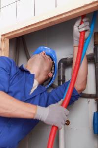 a plumbing contractor feeds a pex pipe up through a wall opening